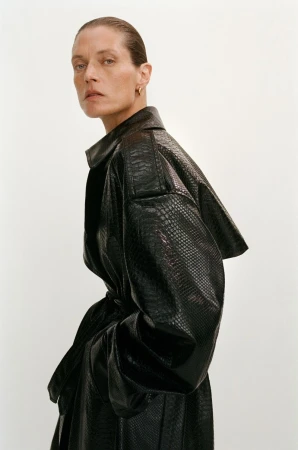 Malgosia Bela wearing an oversized black textured leather trench coat against a white studio background.