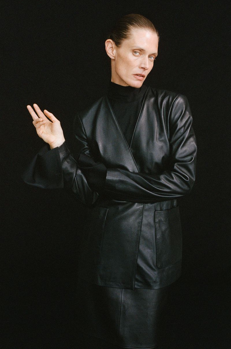 Model Malgosia Bela poses in a black leather jacket and turtleneck against a solid black background.