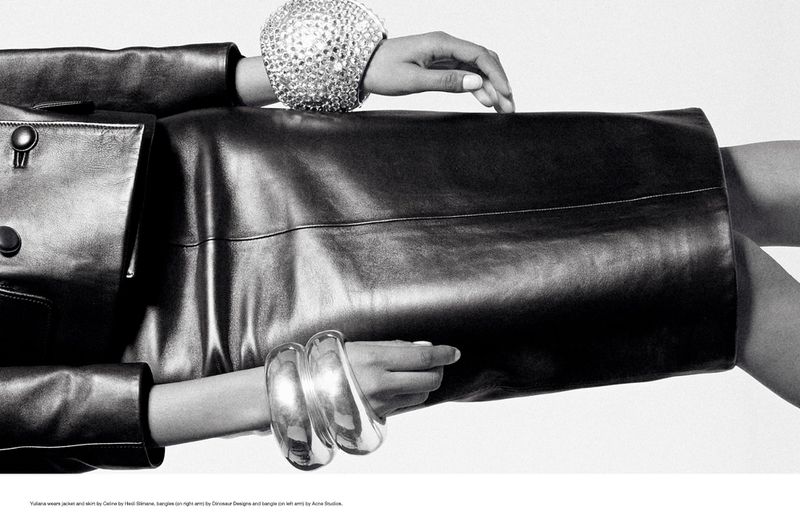 Cropped studio shot of a fair-skinned model wearing a black leather jacket, skirt, and sparkling silver bracelets against a white backdrop.