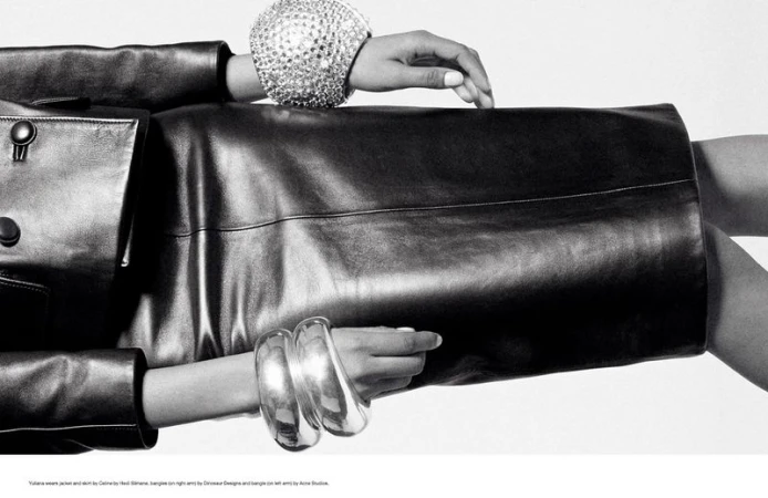 Cropped studio shot of a fair-skinned model wearing a black leather jacket, skirt, and sparkling silver bracelets against a white backdrop.