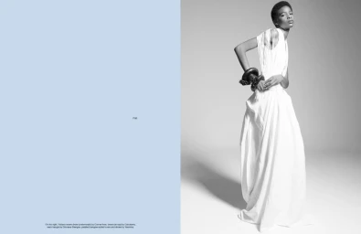 Black and white editorial fashion image featuring a model in a long white dress and chunky bangle against a plain background