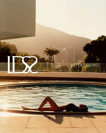 A model reclining beside an outdoor swimming pool during golden hour with palm trees and hills in the background.