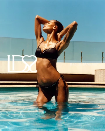 Model Barbara Valente posing in a black bikini in a swimming pool under direct sunlight.