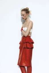 Model in a white strapless top and red ruffled midi skirt with red lace tights posing against a white background.