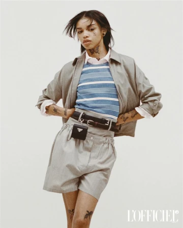 Fashion portrait of a young adult woman with tattoos and casual streetwear in a studio setting with a neutral background.