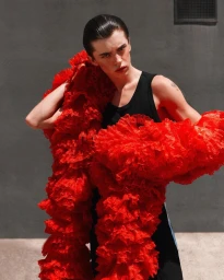 Model in a black tank top wrapped in a voluminous red ruffled fabric scarf outdoors