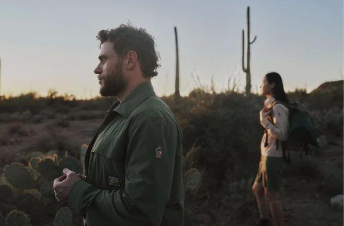 Man in green jacket in profile with a woman standing among desert cacti at sunset for Moncler Grenoble.