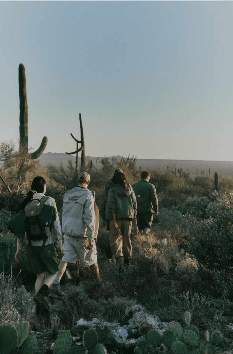 Group of models walking away along a desert trail surrounded by saguaro cacti in Moncler Grenoble outerwear.