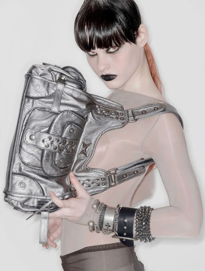 Model with dark eye makeup holding a metallic silver handbag against a white studio background.