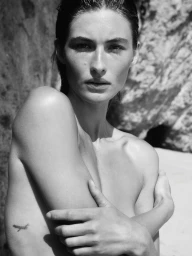 Black and white close-up portrait of model Grace Elizabeth with wet hair and arms crossed against a rocky background.