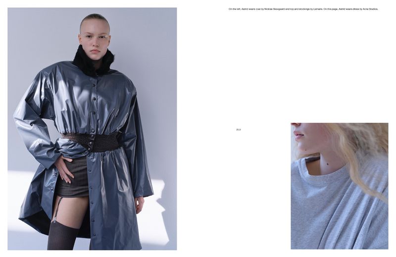 Fashion shot of a female model in a grey coat with a black fur collar and garter belts in a studio against a white background.