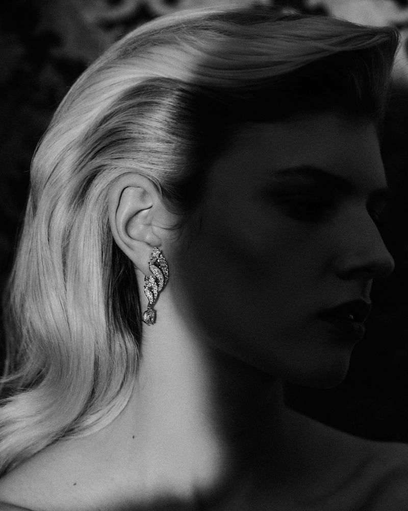 Monochrome close-up profile of model Camille Chifflot wearing an ornate diamond drop earring in chiaroscuro lighting.