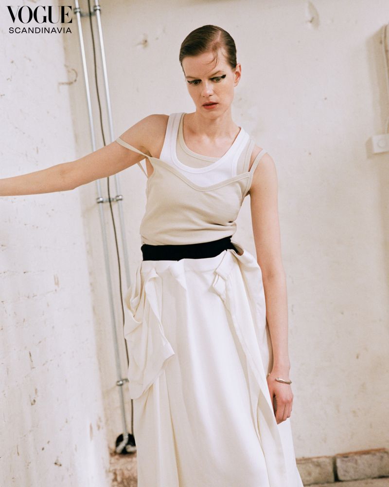 Kadri Vahersalu posing against a pale wall in a beige layered tank top and flowing white maxi skirt for Vogue Scandinavia.