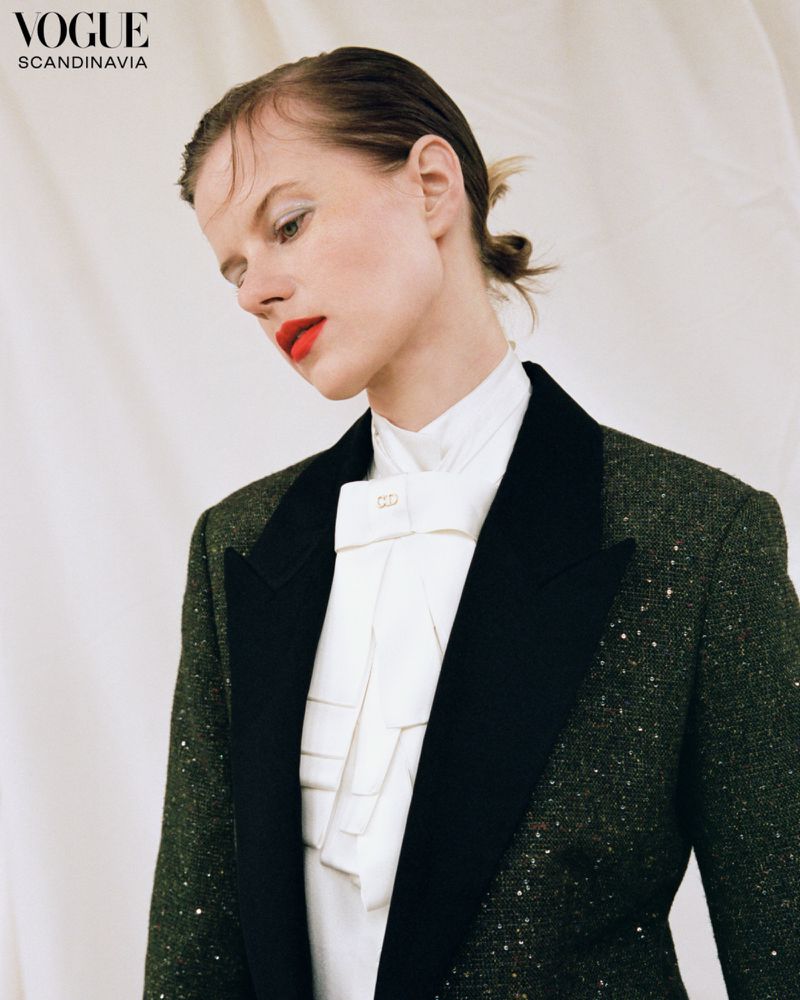Model Kadri Vahersalu in a dark tweed blazer with black lapels and a ruffled white shirt against a neutral draped backdrop.