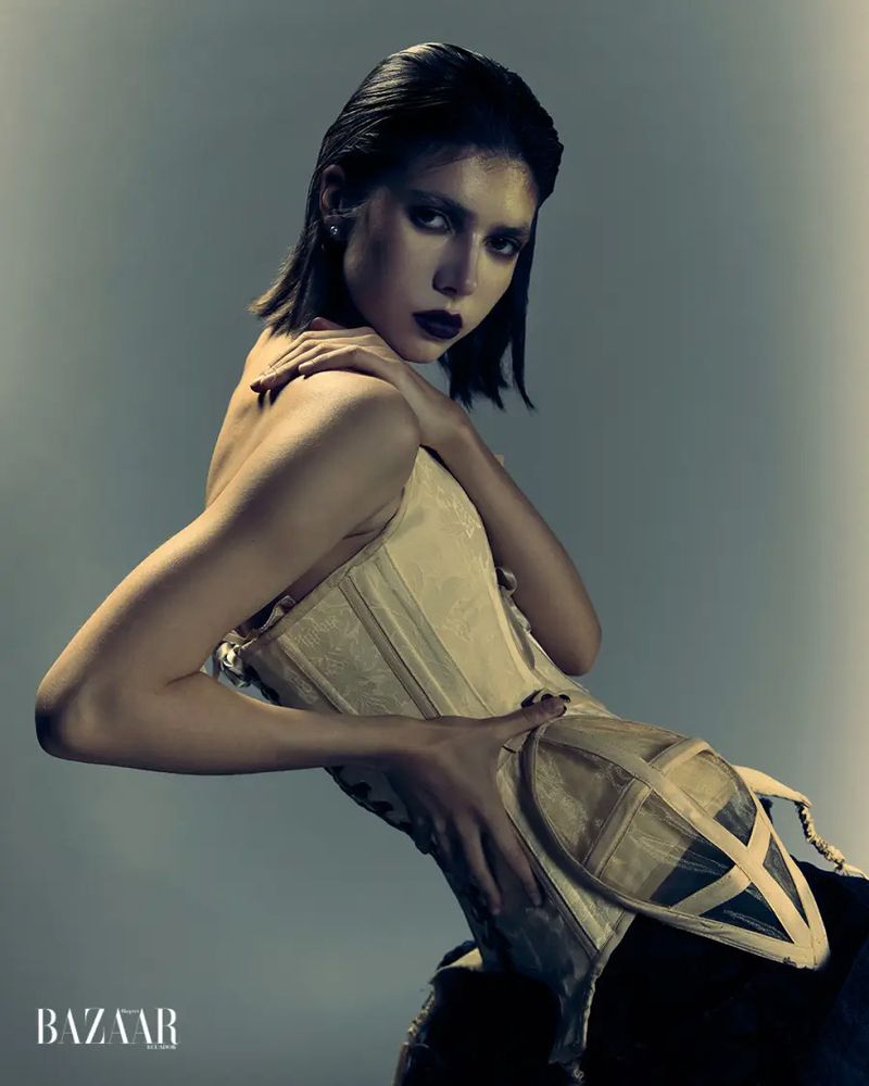 Model posing in a structured cream boned corset with architectural hip cages against a moody grey studio backdrop.
