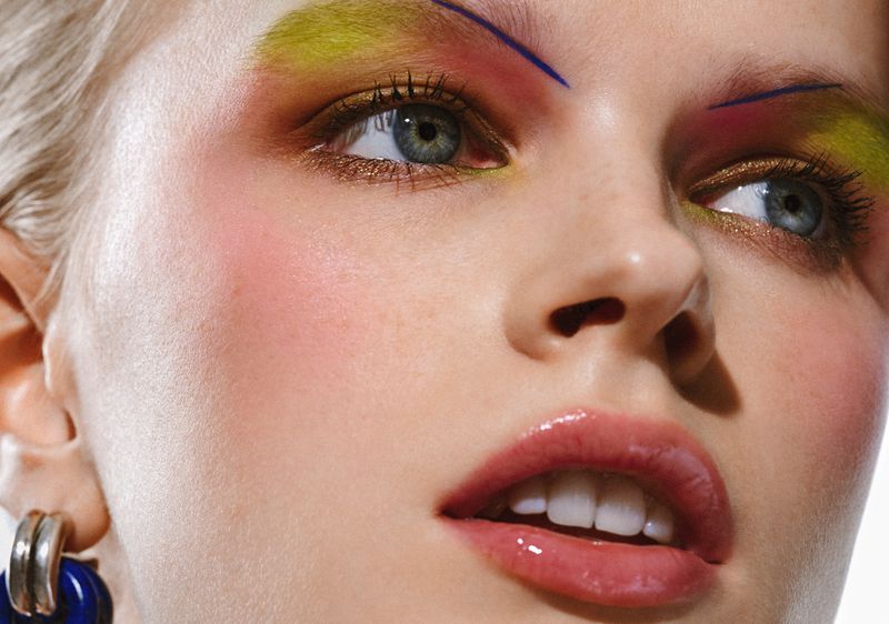 Close-up shot of a woman's face with colorful eye makeup and glossy lips, showcasing beauty and style in a studio environment.