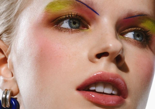 Close-up shot of a woman's face with colorful eye makeup and glossy lips, showcasing beauty and style in a studio environment.