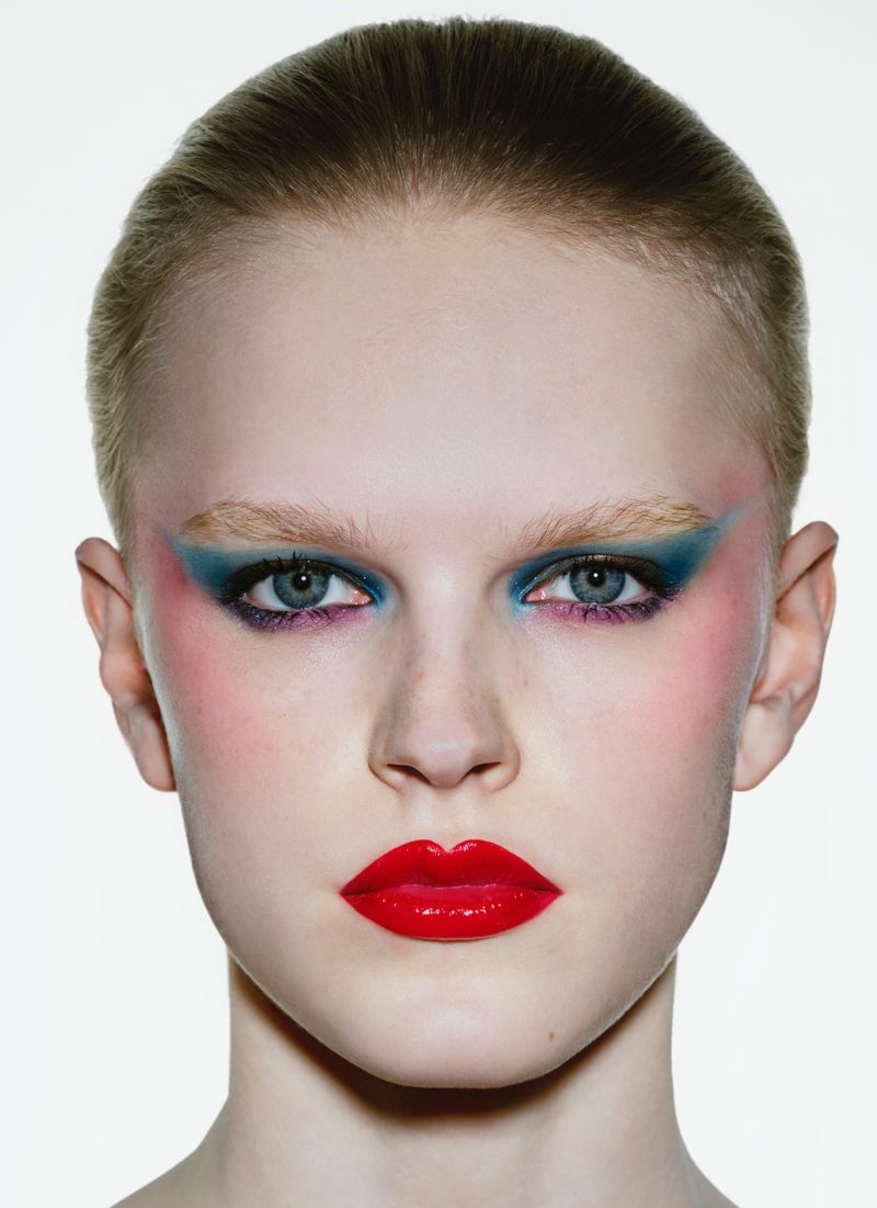 Close-up studio portrait of a fair-skinned young adult woman with colorful makeup (teal eyeshadow, bright red lips). Beauty shot.