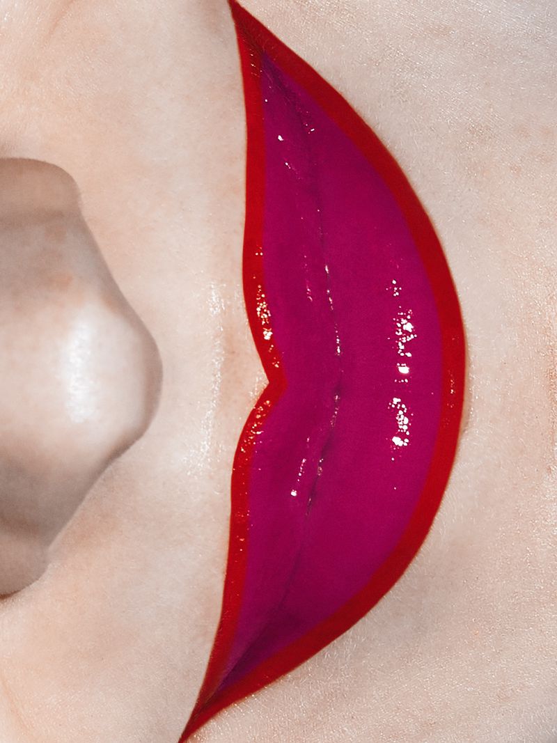 Close-up of a woman's face with glossy magenta lips and a vibrant red lip liner, showcasing beauty and makeup artistry.