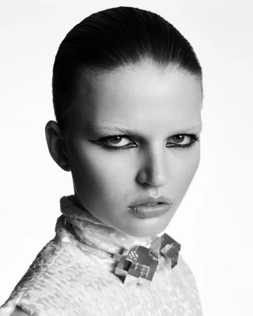 Close up portrait of a woman with slicked back hair and winged eyeliner wearing a patterned high collar top against a plain white background