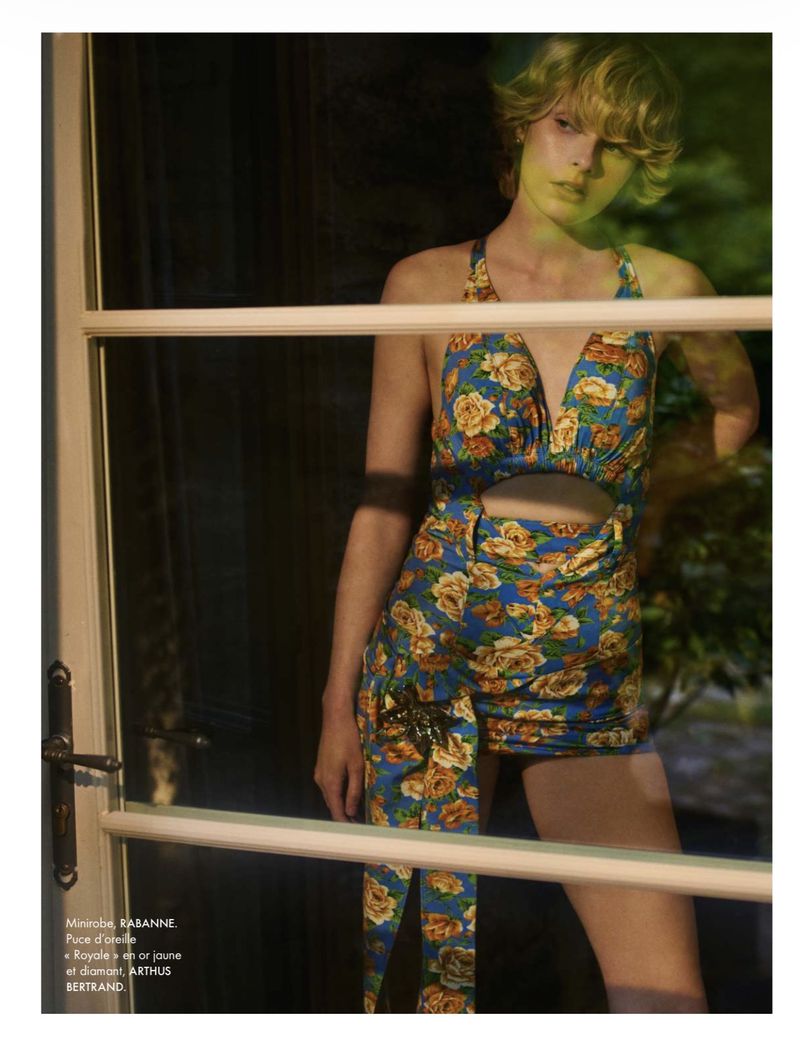 Model wearing a blue floral cutout minidress standing behind a glass door for Elle France