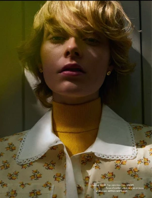 Close-up portrait of model Em Verleun wearing a yellow turtleneck and floral print shirt with white lace collar.