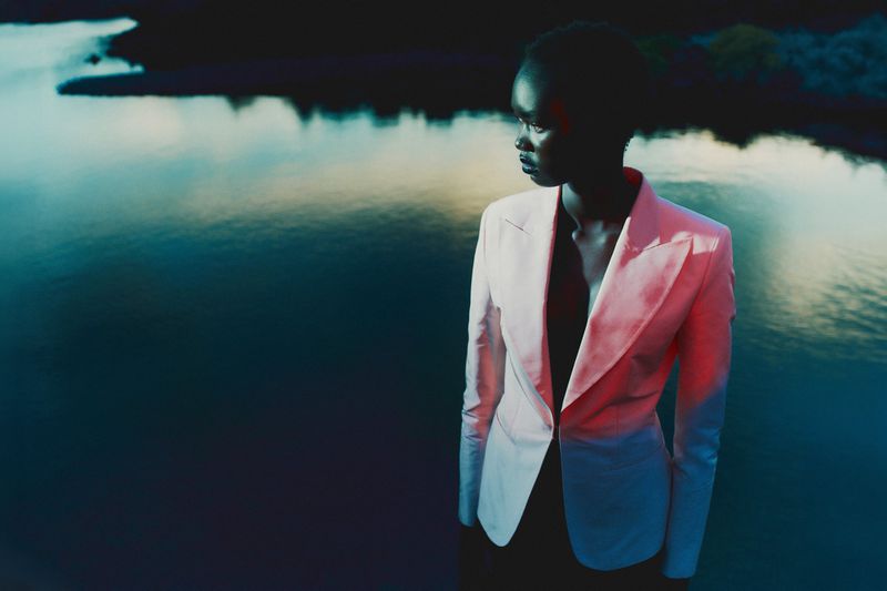 Black model wearing a light pink blazer standing outdoors near water at dusk for Seduction Magazine