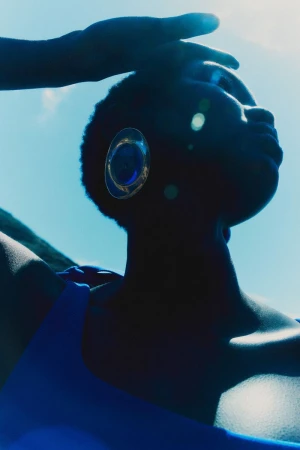 Model Ateta Jok wearing a bright blue top and large silver circular earring against a bright blue sky.