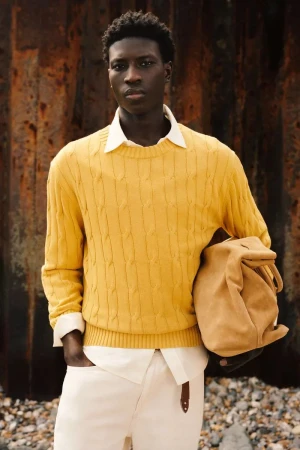 Model Cheikh Amar Diaw wearing a yellow cable-knit sweater and white trousers with a tan bag for Zara Origins.