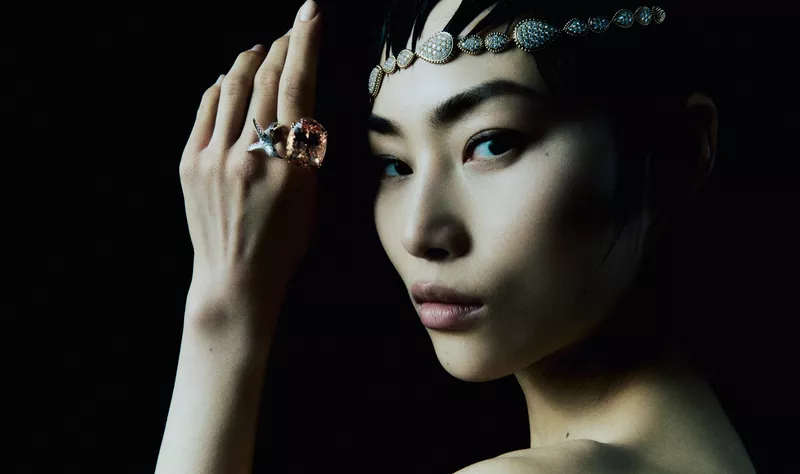 East Asian model Wawa Li wearing a diamond headpiece and large gemstone ring against a solid black background.