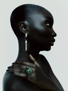 Profile portrait of model Diarra Ndiaye wearing a sparkling drop earring and an intricate green cluster ring against a studio backdrop.