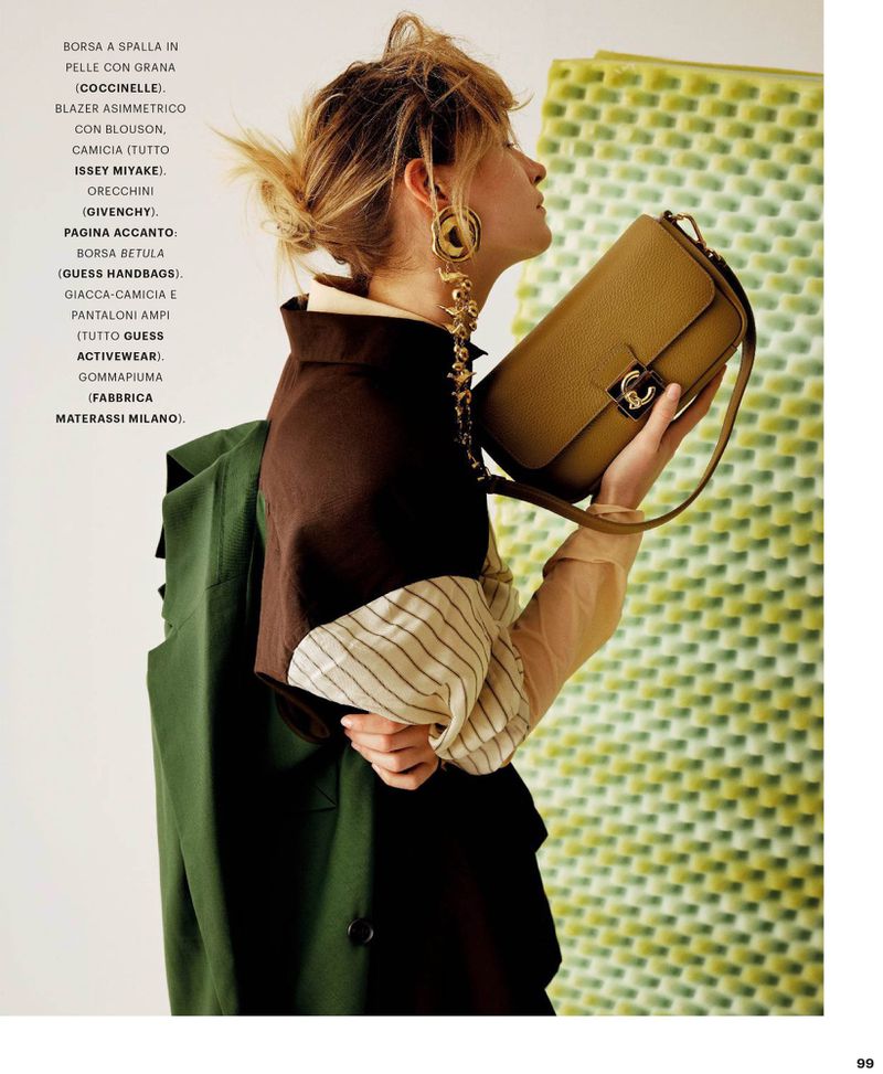 Woman in profile holding a tan leather shoulder bag, wearing layered brown and green garments and large gold drop earrings.