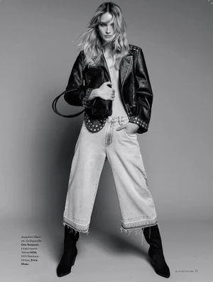 Model in an open studded leather jacket, wide-leg cropped jeans, and black boots posing against a studio backdrop.