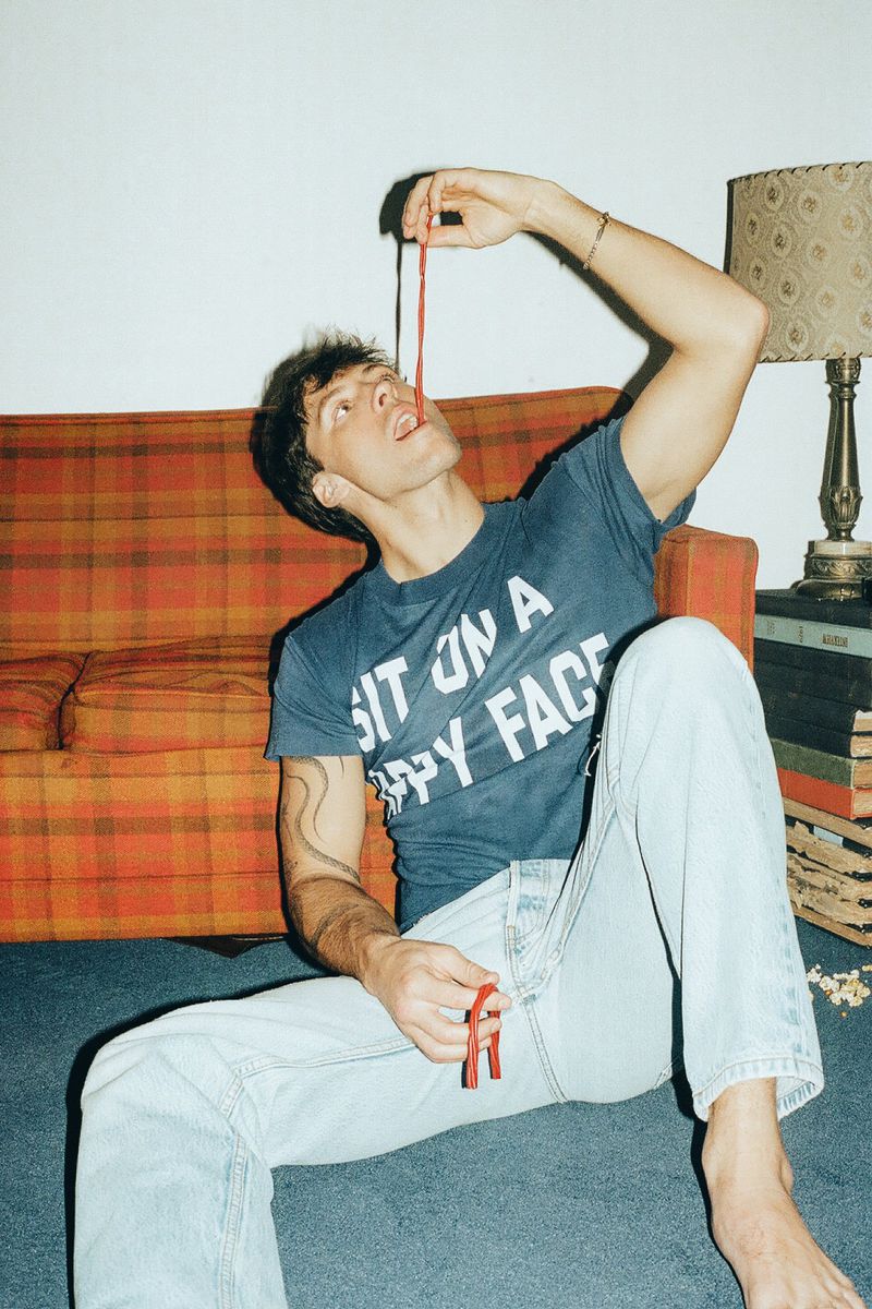 Rob Rausch sitting on the floor leaning against a plaid sofa while eating a strand of red licorice candy.