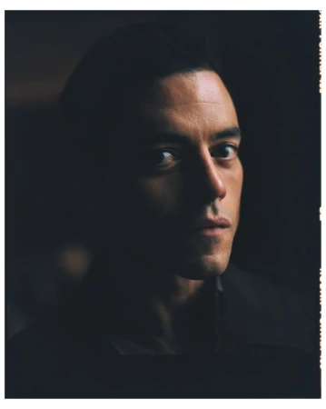 Close-up portrait of an adult male with short dark hair, looking forward in a photo studio with dark lighting and neutral background.