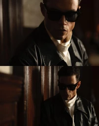Portrait of Rami Malek wearing dark sunglasses, a black jacket, and a white collared shirt against a dark wood background.