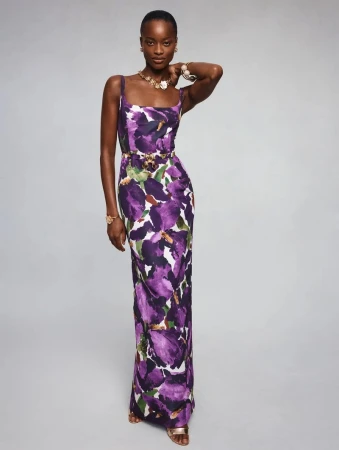 Model Mayowa Nicholas wears a purple floral maxi dress with gold jewelry against a grey studio backdrop for Oscar de la Renta.
