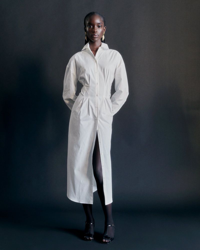 Model Maty Fall wearing a long white buttoned dress against a dark backdrop for Sezane