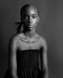 Monochrome portrait of model Maty Fall wearing a strapless pleated black top against a seamless studio backdrop.
