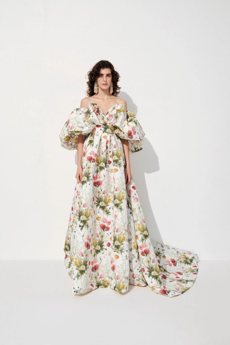 Model wearing an off-the-shoulder floral print ballgown with voluminous puff sleeves and a train against a white background.