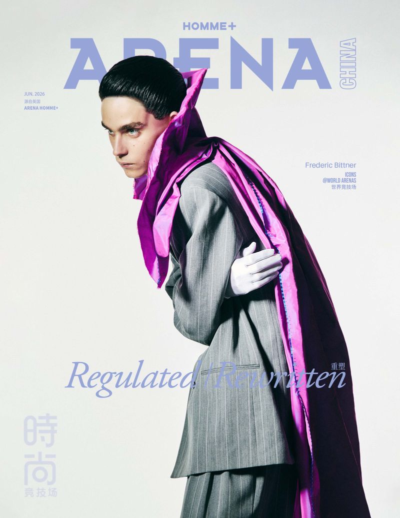 Model Frederic Bittner poses in a grey pinstriped suit and sculptural purple cape against a white studio background.