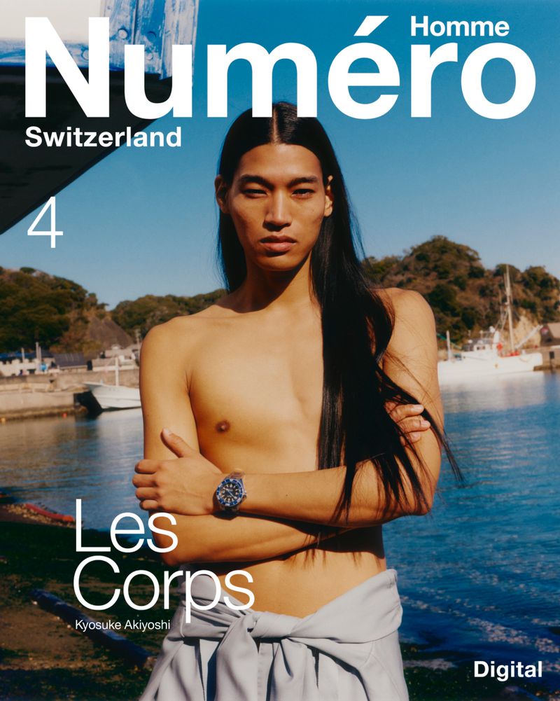 Model Kyosuke Akiyoshi shirtless with long black hair posing in front of a coastal harbor for Numéro Homme Switzerland.