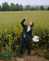 Walton Goggins wearing a dark grey suit and holding a cake in a yellow field for the Paul Smith AW 26 campaign.