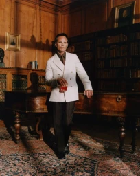 Actor Walton Goggins wearing a white double-breasted blazer and holding a drink in a wood-paneled library.