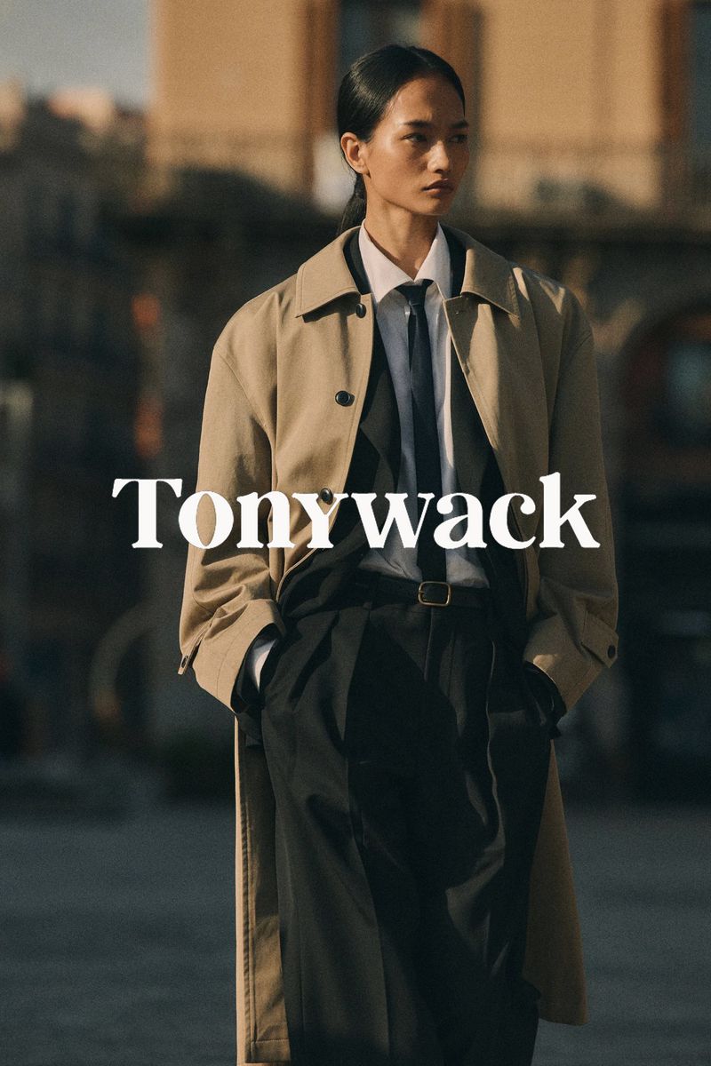 Model Mona Bhujel wearing an oversized beige trench coat, white shirt, black tie, and dark trousers for Tonywack.