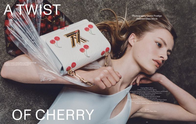 Fashion editorial featuring a model lying next to a white purse with cherry details, accessorized with plastic and real cherries.