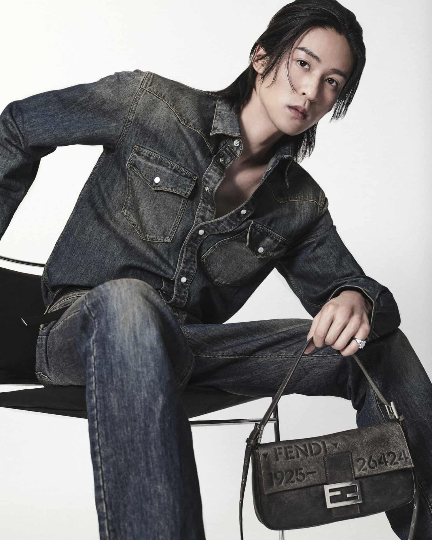 Ren Meguro wearing a dark denim shirt and jeans while holding a black Fendi Baguette bag against a white background.