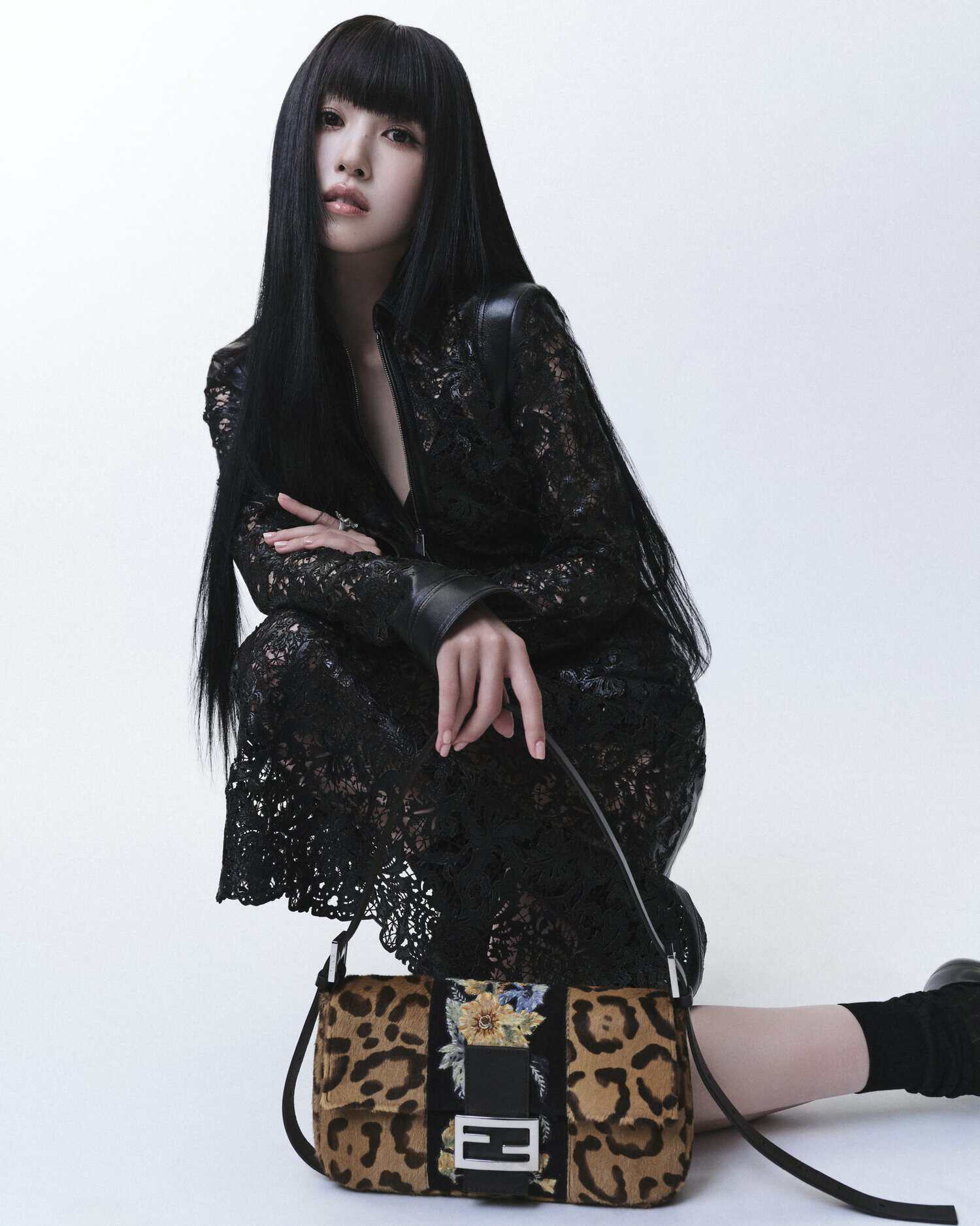 Song Yuqi crouching in a black lace dress next to a leopard print Fendi Baguette bag against a white studio background.