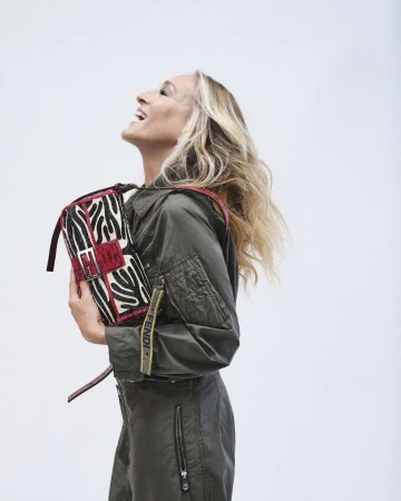 Sarah Jessica Parker wearing an olive green jumpsuit holding a patterned Fendi Baguette shoulder bag against a white background.
