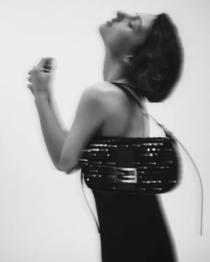Monochrome portrait of a woman in a black dress posing with an embellished black Fendi Baguette shoulder bag on a white backdrop.